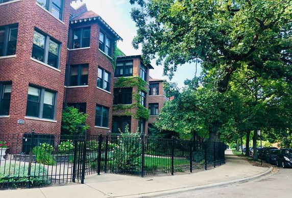Front view of a brick apartment building with multiple floors and a black iron fence.