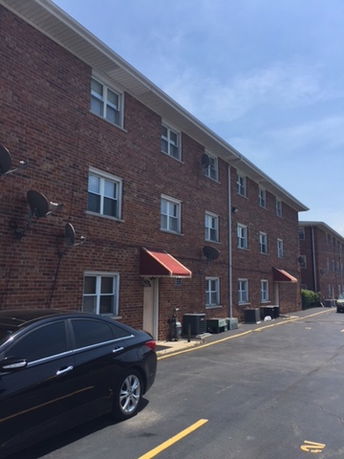 Front view of a three-story brick apartment building with awnings over entrances.