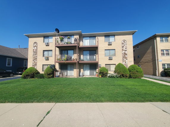 Front view of a multi-story apartment building with balconies and a well-maintained lawn.