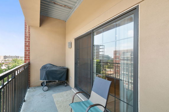 Balcony with a barbecue grill and chair, overlooking surrounding buildings.