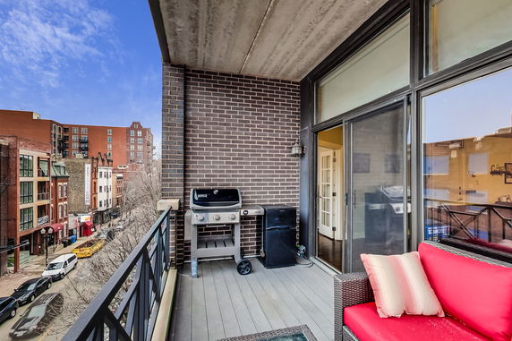Balcony with a barbecue grill overlooking surrounding buildings and street.