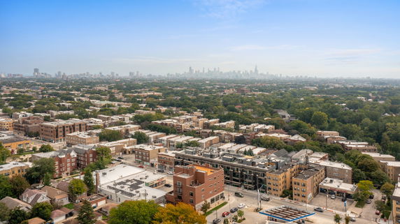 Panoramic view of an urban area with buildings and trees, overlooking a city skyline in the distance.
