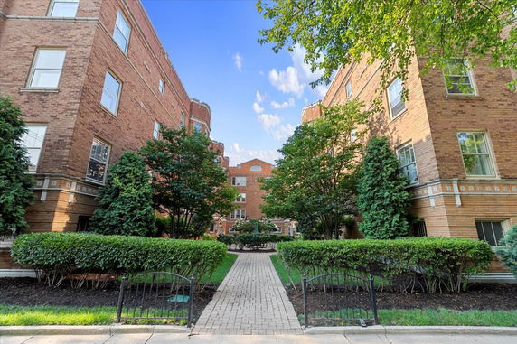 Front view of a brick multi-story building with a central pathway and greenery.