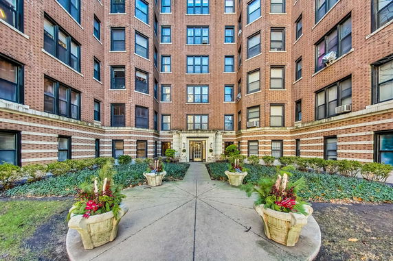 Front view of a multi-story brick apartment building with decorative planters.