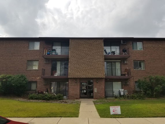 Front view of a three-story brick apartment building with balconies.