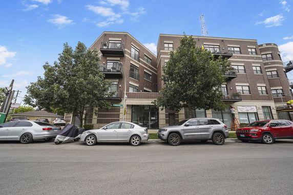 Front view of a multi-story brick building with balconies and parked cars.