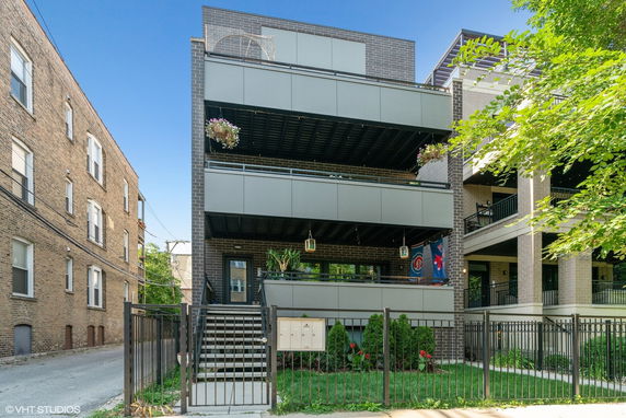 Front view of a modern multi-story building with balconies and a gated entrance.