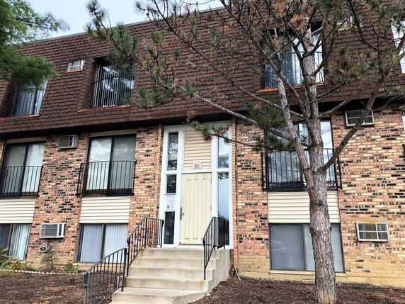 Front view of a multi-story brick apartment building with a central entrance and large windows.