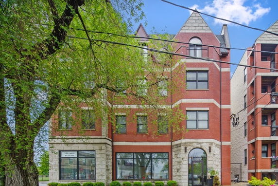 Front view of a multi-story brick building with large windows and a peaked roof.