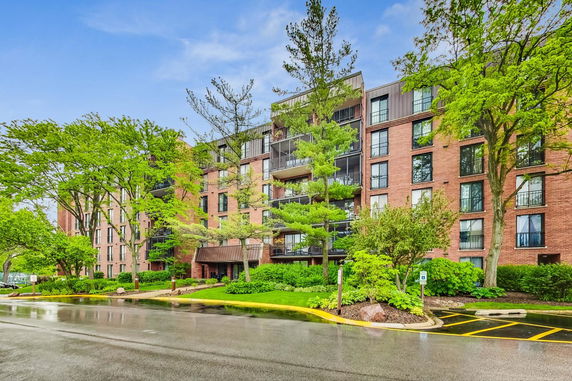 Front view of a multi-story brick apartment building with balconies and surrounding trees.