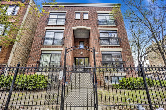 Front view of a three-story brick building with balconies and a gated entrance.
