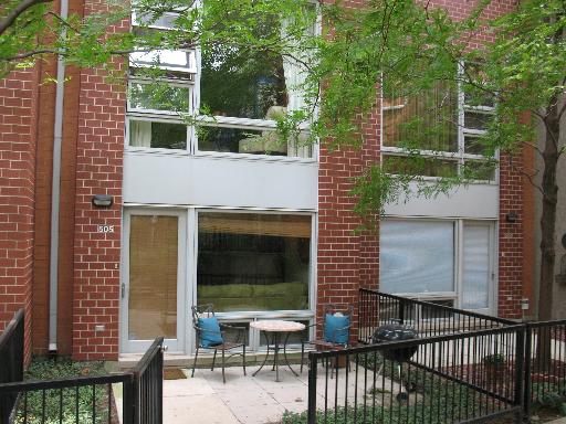 Front view of a brick apartment building with large windows and a small patio area.