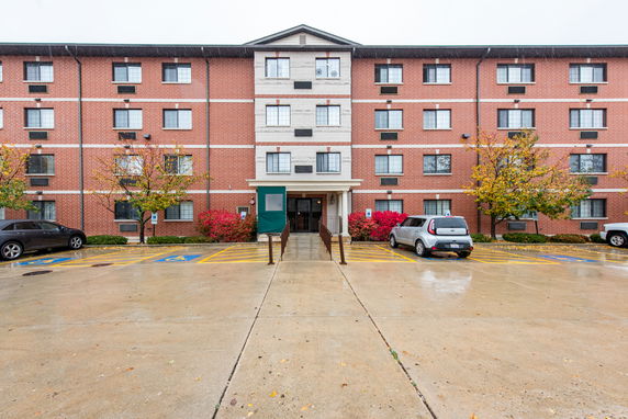 Front view of a multi-story brick building with a central entrance and parking area.