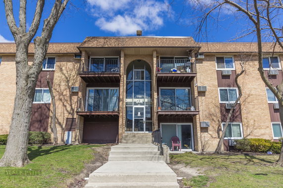 Front view of a multi-story brick apartment building with balconies and central glass stairway entrance.