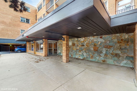Front view of a brick building entrance with stone wall and covered walkway.