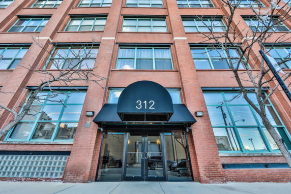 Front view of a multi-story brick building with large windows and a black entrance canopy.