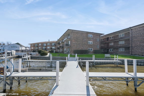 Front view of multi-story brick residential buildings with balconies, seen from a dock on the water.