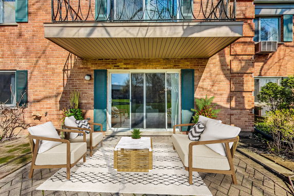 Front view of a brick house with a balcony and patio seating area.