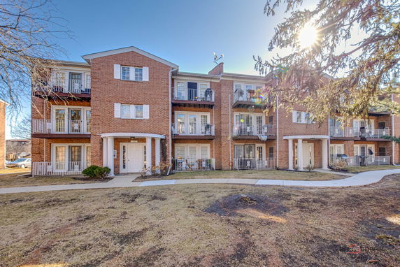 Front view of a three-story brick apartment building with balconies.