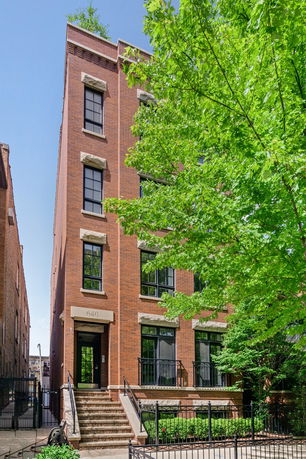 Front view of a multi-story brick building with large windows and an entrance flanked by stairs.