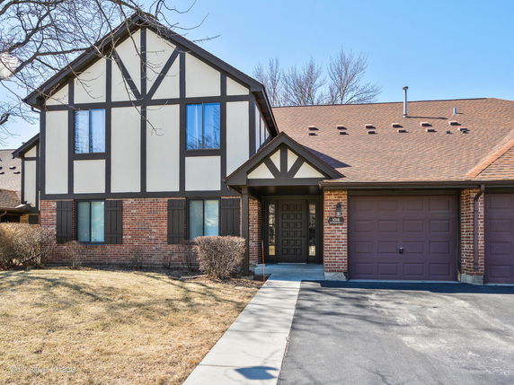 Front view of a two-story house with brick and wood paneling and an attached garage.