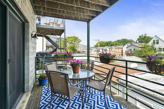 A balcony with outdoor furniture and plants, overlooking residential neighborhood.