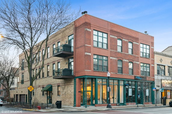 Front view of a three-story brick corner building with large windows and balconies.