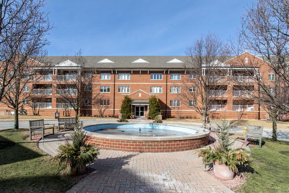 Front view of a large multi-story brick building with balconies and a central fountain.
