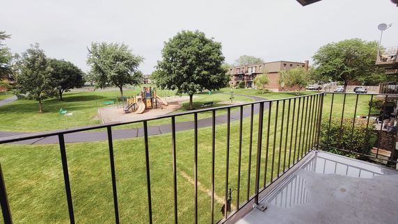 View of a playground and green area with surrounding buildings seen from a balcony.