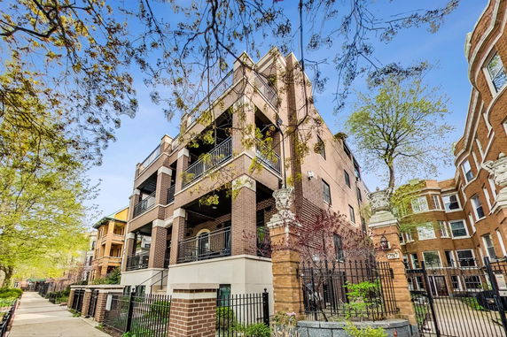 Front view of a multi-story brick building with balconies and a gated entrance.