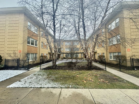Front view of a multi-story brick building with a central entrance and fenced pathways.