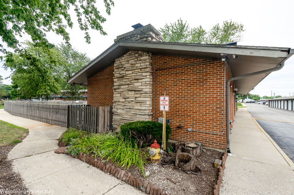 Side view of a brick building with a chimney and sloped roof.