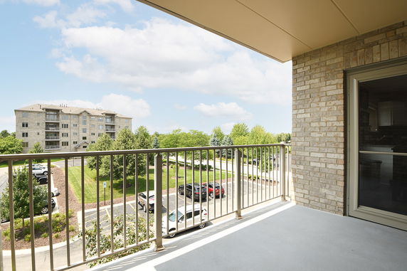 View from a balcony overlooking a parking lot and an apartment building.