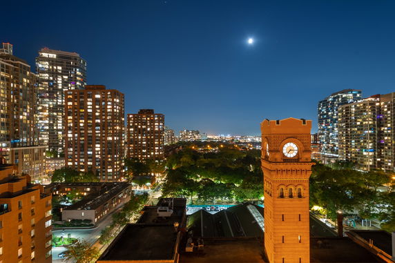 Nighttime panoramic view of city buildings with a clock tower and illuminated windows.