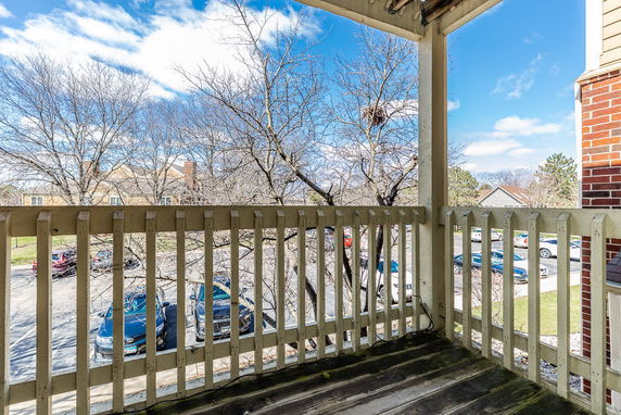 View from a balcony overlooking a parking area with bare trees and buildings in the distance.
