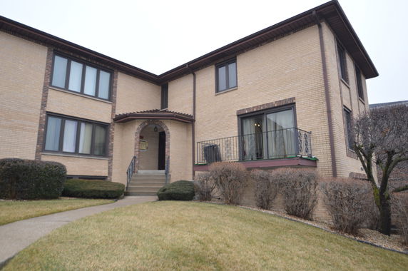 Front view of a two-story house with beige brick exterior and arched entryway.