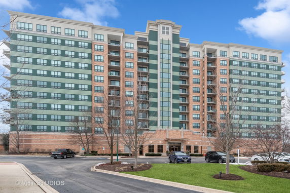 Front view of a mid-rise apartment building with multiple levels and a parking area in front.