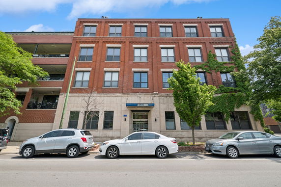 Front view of a four-story red brick building with parked cars in front.