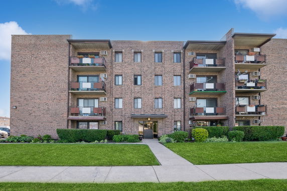Front view of a multi-story brick apartment building with balconies.