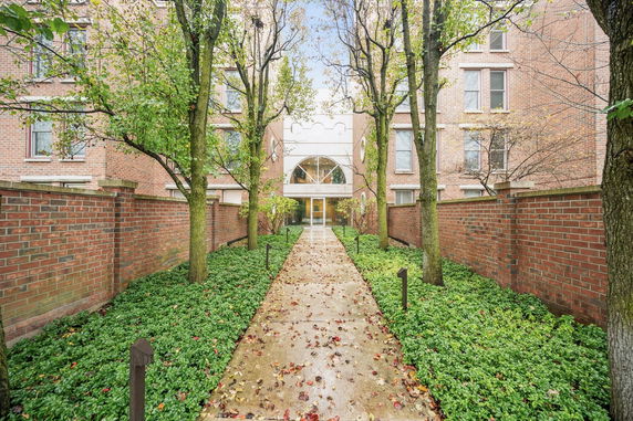 Front view of a brick building with an entrance pathway lined with greenery and trees.