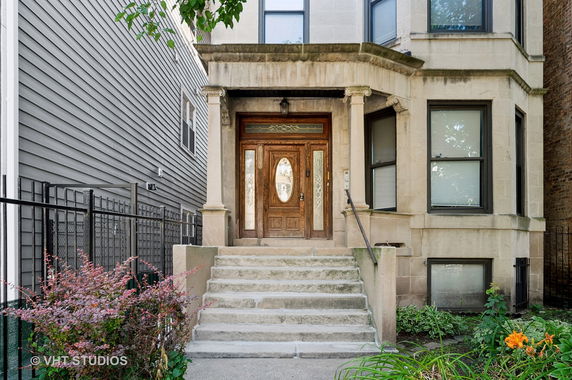 Front view of a stone townhouse with a wooden door and steps leading up to the entrance.