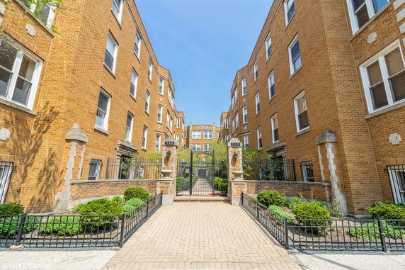 Front view of a multi-story brick apartment building with a gated entrance.