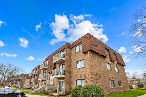 Front view of a three-story brick apartment building with balconies.