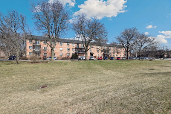 Front view of a multi-story brick building with balconies and parked cars.