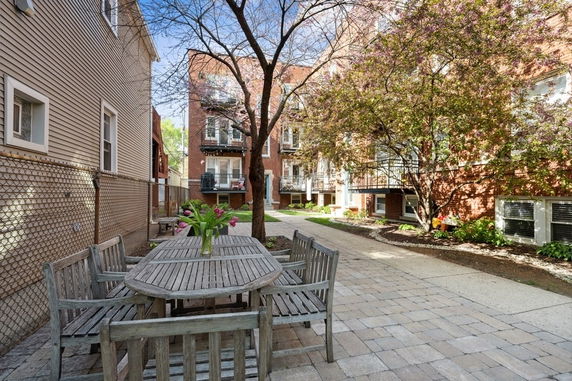 Outdoor area with wooden table and chairs in a courtyard surrounded by brick buildings.