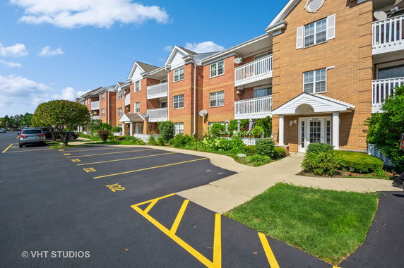 Front view of a multi-story brick apartment building with balconies and a parking area.
