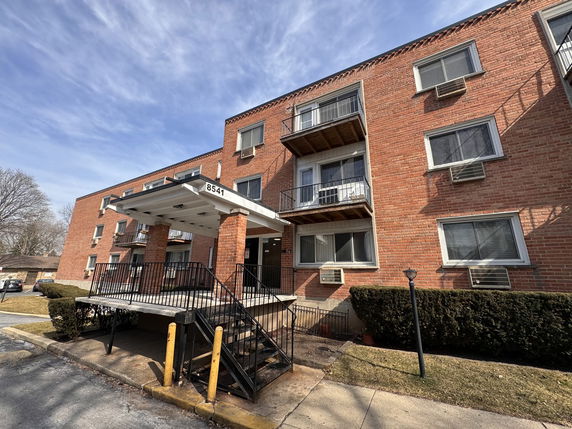 Front view of a multi-story brick building with balconies and a covered entrance.