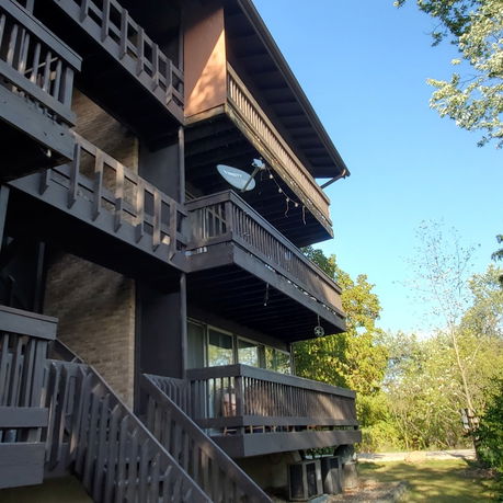 Side view of a multi-story building with dark wooden balconies and external stairs.