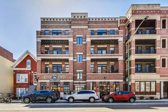 Front view of a multi-story brick building with balconies and a tattoo shop on the ground floor.