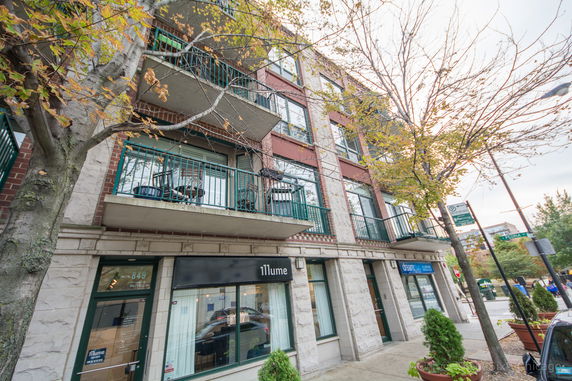 Front view of a multi-story building with balconies and retail space on the ground floor.